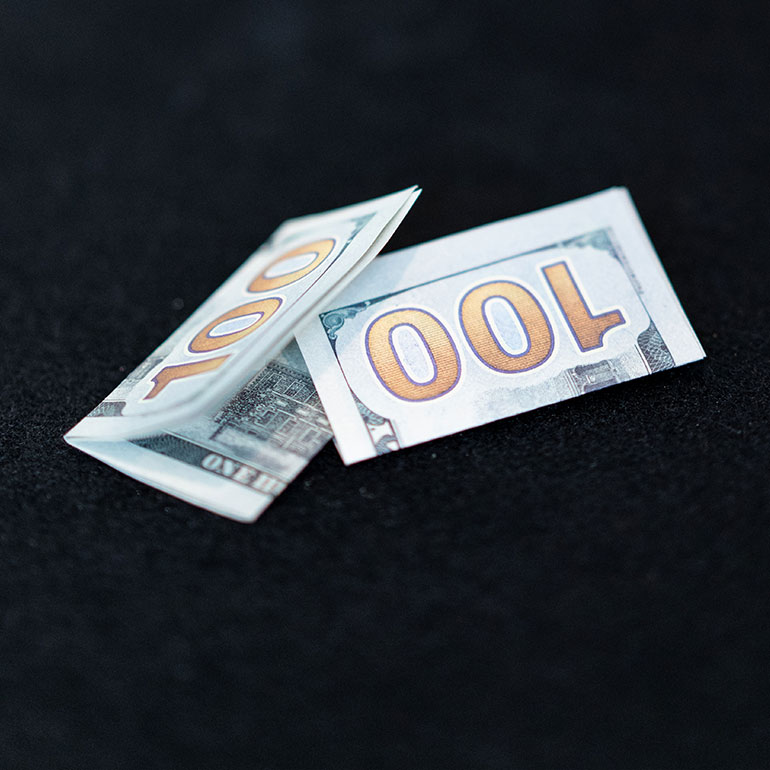 2 folded 100 dollar bills on a black background.